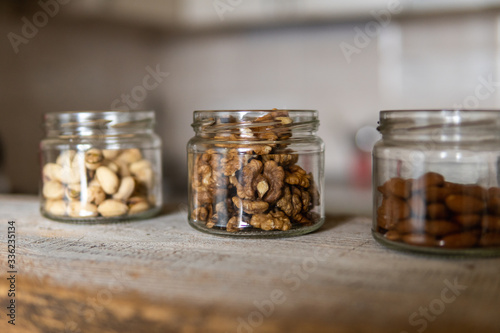 Almond, walnut and pistachio in a jars which standing on a white vintage table with a kitchen on background. Nuts is a healthy vegetarian protein and nutritious food. Nuts on rustic old wood.