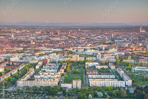 Aerial view of Munich outskirts and historic center Altstadt at sunset with  housing estates, office buildings, green parks, church towers and snowy Bavarian Alps in background, Bayern Germany Europe © nogreenabove2k