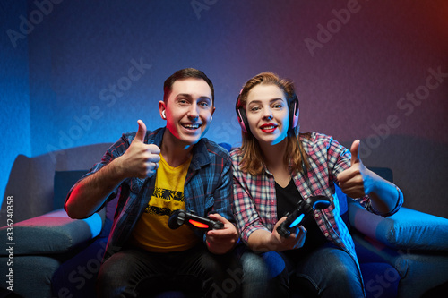 Portrait of crazy playful couple, Gamers enjoying Playing Video Games on Playstation indoors sitting on the sofa, holding Console Gamepad in hands, Xbox fans. Resting At Home, have a great Weekend