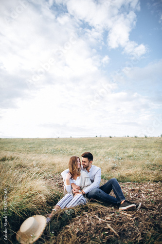 Lovely   ouple hugging  kissing and smiling against the sky seating on grass. Space for text