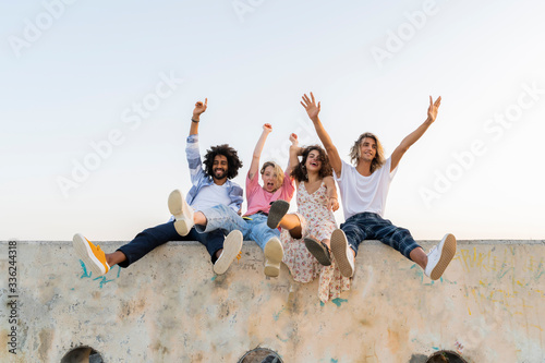 Portrait of happy friends sitting on a concrete wall outdoors photo