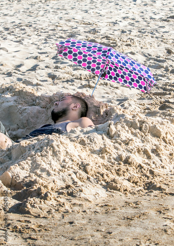 Man relaxing in a cool hole dug in the sand