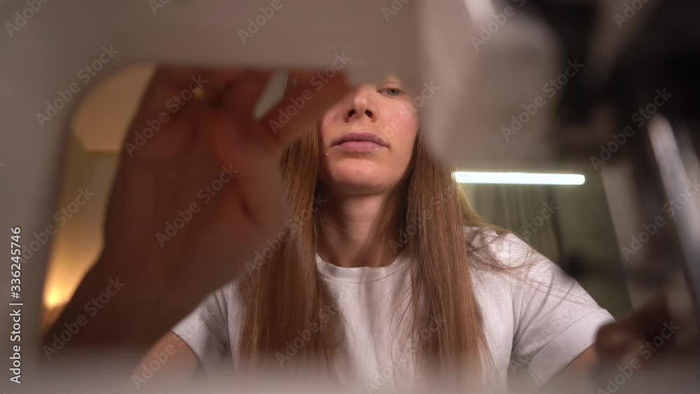 Woman in a white T-shirt sews on a sewing machine. Cuts black threads with scissors. Woman works in an apartment with a modern interior. Close-up. Wide angle.