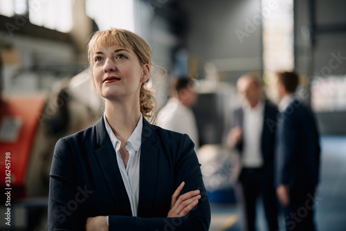 Portrait of a confident businesswoman in a factory with colleagues in backgound