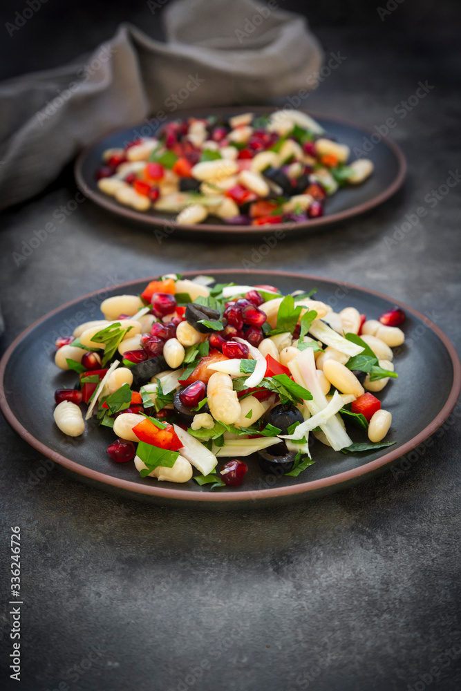 Two plates of?cannellini?bean salad with fennel, bell pepper, black olives, pomegranate seeds, mint and parsley Two plates of?cannellini?bean salad with fennel, bell pepper, black olives, pomegranate seeds, mint and parsley