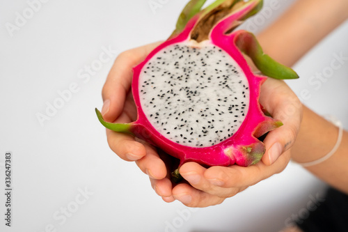 Female hands holding a half of the ripe white dragon fruit on white background.