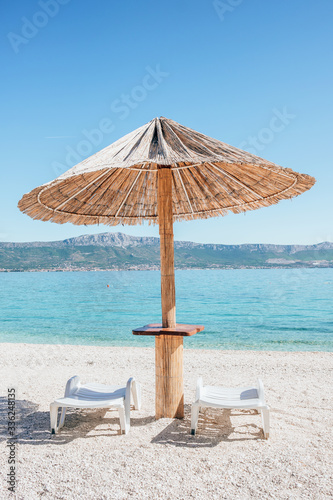 Fototapeta Naklejka Na Ścianę i Meble -  Summer straw umbrella and two sun beds at empty beach in Croatia.
