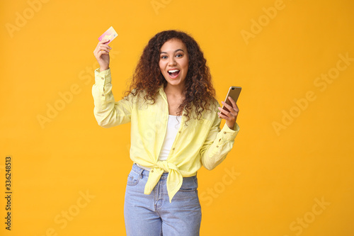 Happy woman with mobile phone and credit card on color background. Online shopping concept