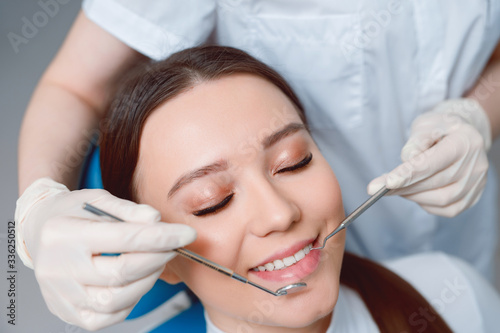 Fototapeta Naklejka Na Ścianę i Meble -  Patient in dental chair. Dentist's hands with blue gloves work with a dental tools. Beautiful young woman having dental treatment at dentist's office.