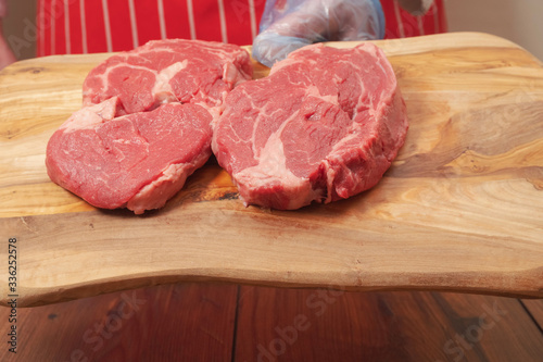 Proffesional butcher holding wooden cutting board with two fresh rib eye steaks. Meat industry concept.