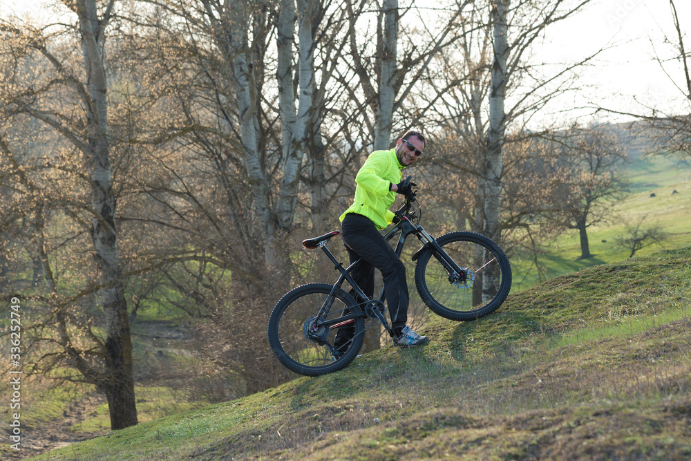 Cyclist in pants and green jacket on a modern carbon hardtail bike with an air suspension fork. The guy on the top of the hill rides a bike. Cyclist in pants and green jacket on a modern carbon hardtail bike with an air suspension fork. The guy on the top of the hill rides a bike.