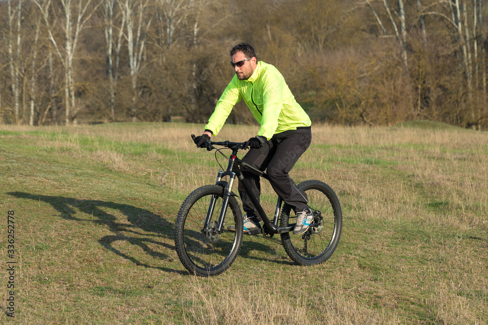 Cyclist in pants and green jacket on a modern carbon hardtail bike with an air suspension fork. The guy on the top of the hill rides a bike.