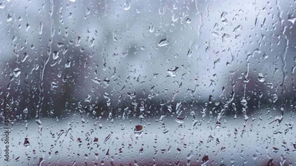 Raindrops sitting and dripping slowly on a window on a grey day with blurry apartments in the background. Raindrops sitting and dripping slowly on a window on a grey day with blurry apartments in the background.