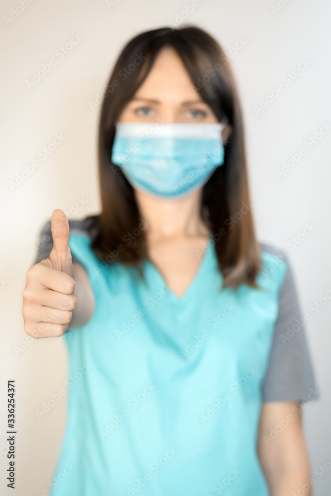 The topic of coronavirus and safety. Young female surgeon with dark hair in a mask from a virus shows thumb up. Vertical frame The topic of coronavirus and safety. Young female surgeon with dark hair in a mask from a virus shows thumb up. Vertical frame