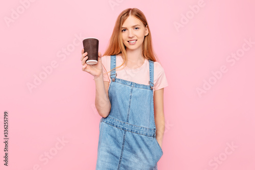 stylish young woman in casual clothes, posing with coffee in hand, on an isolated pink background