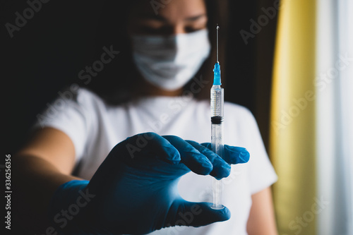 Nurse in a medical mask and gloves hold a syringe