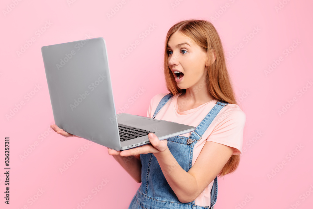 Naklejka premium Portrait of a shocked girl holding a laptop isolated on a pink background