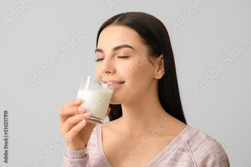 Beautiful young woman drinking milk on light background