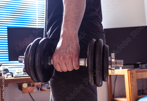 Closeup to a young man holding and squeezing an iron dumbbel with room background.  Ideal for fitness, sports, home workout, excerside indoor and  healthy life.  photo