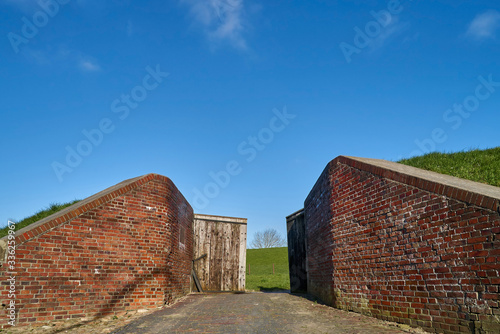  Historical sluice gate in front of the dike at Abser Siel in Stadland-Rodenkirchen (district Wesermarsch, Germany) against a blue sky on a sunny day