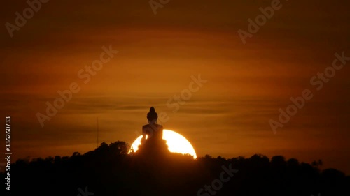 hue sunset behind silhouette Phuket big buddha statue on hilltop with many big trees high mountain in the beautiful evening colourful  orange twilight sky , attraction tourist photo spot