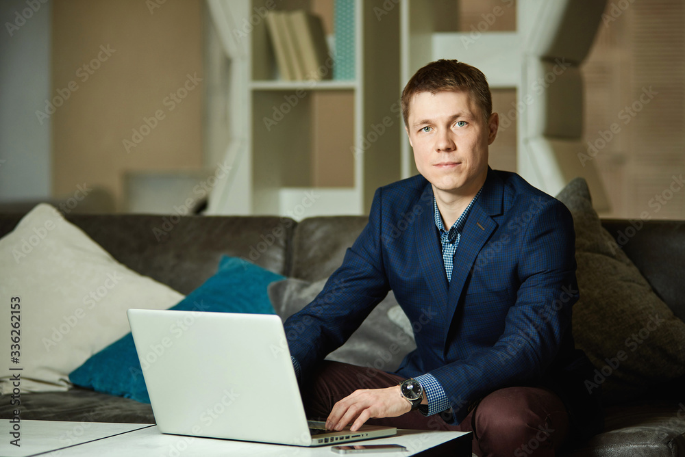 Portrait of a young businessman sitting at a table and typing on a laptop, looking at camera. Portrait of a young businessman sitting at a table and typing on a laptop, looking at camera.