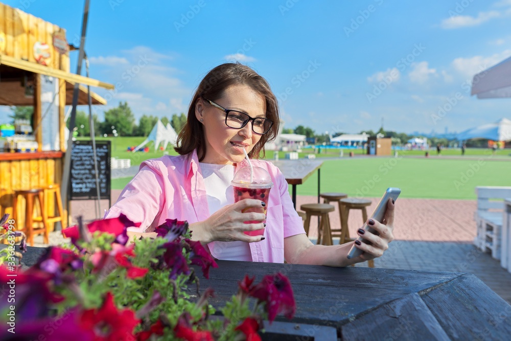Fototapeta premium Summer portrait of mature woman with drink and smartphone