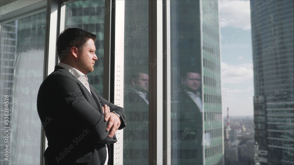 Hard times for a businessman and his business. Thoughtful businessman portrait in his office near a window. Businessman worries about his business standing near the window Hard times for a businessman and his business. Thoughtful businessman portrait in his office near a window. Businessman worries about his business standing near the window