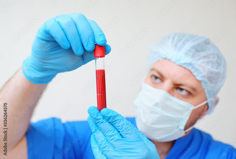 a test tube with a blood sample in the hands of a doctor in blue rubber gloves and a mask on a light background. Concept of coronavirus, covid-19 a test tube with a blood sample in the hands of a doctor in blue rubber gloves and a mask on a light background. Concept of coronavirus, covid-19