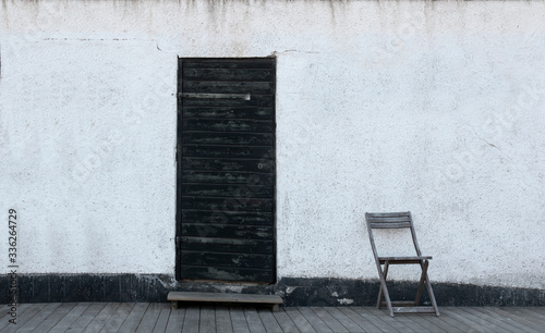 Fotografi Sparse image with white wall, black vintage wooden door with peeling paint and s
