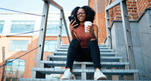 Young content black woman browsing smartphone in street