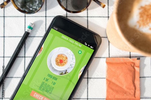 top view orderfood online delivery on mobile screen with coffee cup,sunglasses,pencil on white table cloth.work from home concept photo