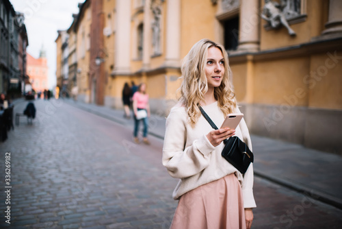 Thoughtful adult stylish female surfing smartphone on street