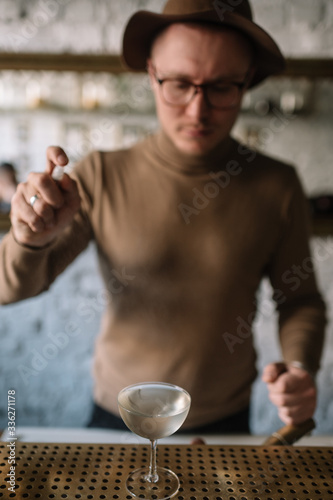 Bartender preparing cocktail based on gin  birch juice cordial and spraying essential oil of frankincense into a glass with cocktail.