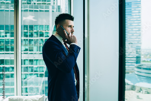 Thoughtful businessman talking on smartphone near window
