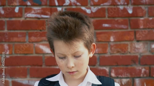 Handsome little boy a pupil in white school suit puts on protective face mask from corona virus on red brick wall background on sunny day outdoor close up slow motion. Isolation period in the world. photo