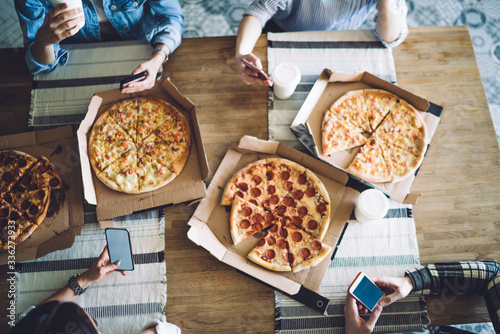 Tasty round pizza in box on table for friends with smartphone