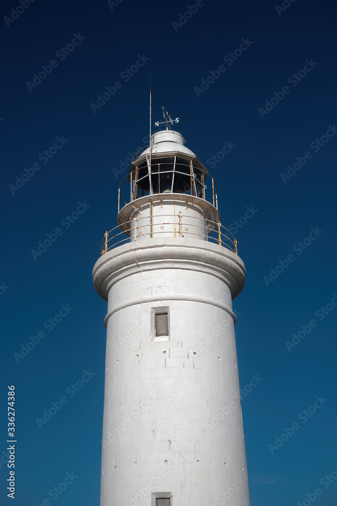 White lighthouse against a blue sky a signal for caution of ships sailing in the sea.