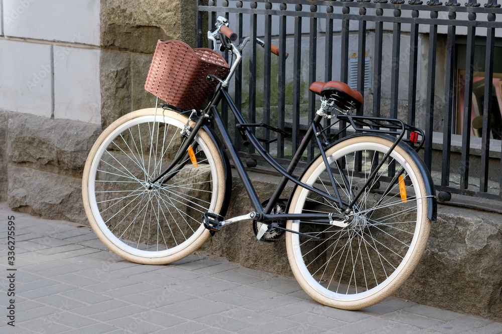 A leisure bike with a brown basket is parked near a metal fence. City bike for walking and shopping trip. Bicycle theft unreliable locks.
