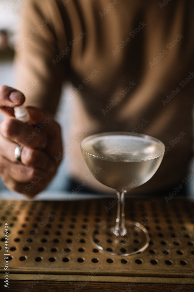 Bartender preparing cocktail based on gin, birch juice cordial and spraying essential oil of frankincense into a glass with cocktail. Bartender preparing cocktail based on gin, birch juice cordial and spraying essential oil of frankincense into a glass with cocktail.