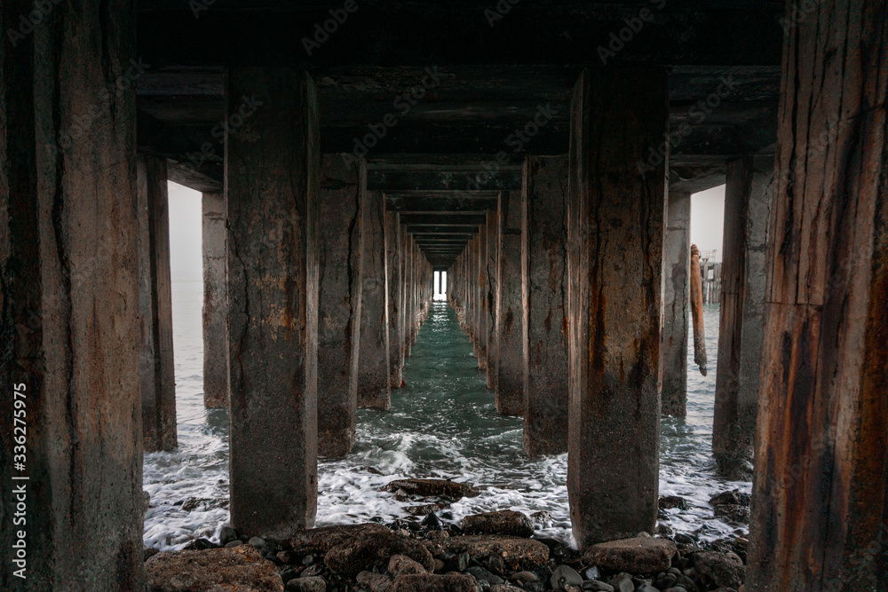 Low light structure view under pier with calm water splashing on rocks. 