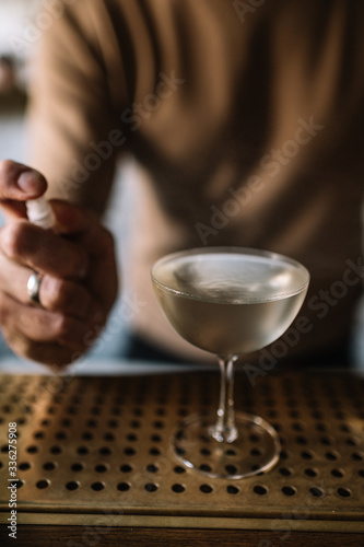 Bartender preparing cocktail based on gin, birch juice cordial and spraying essential oil of frankincense into a glass with cocktail.