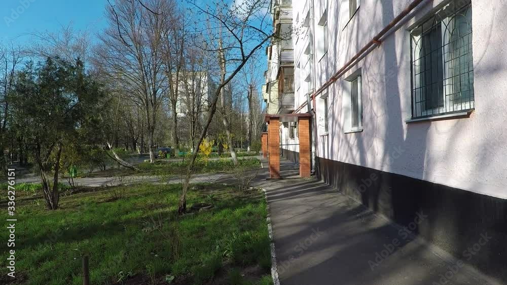 movement with a camera along the entrances of the apartment building, the beginning of spring, grass, trees, flowers.