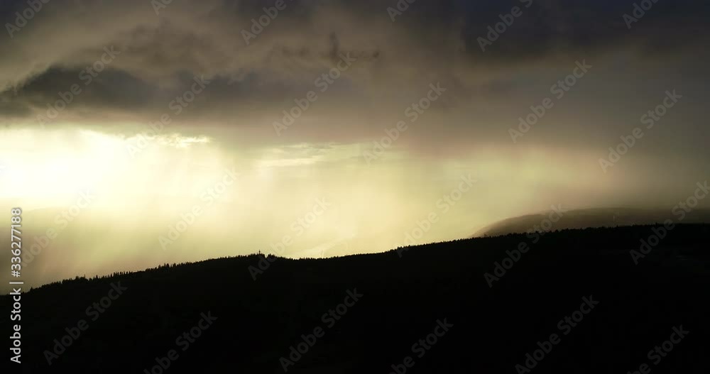 Aerial view of epic dramatic storm and rain over idyllic beautiful valley and mountains during sunset.