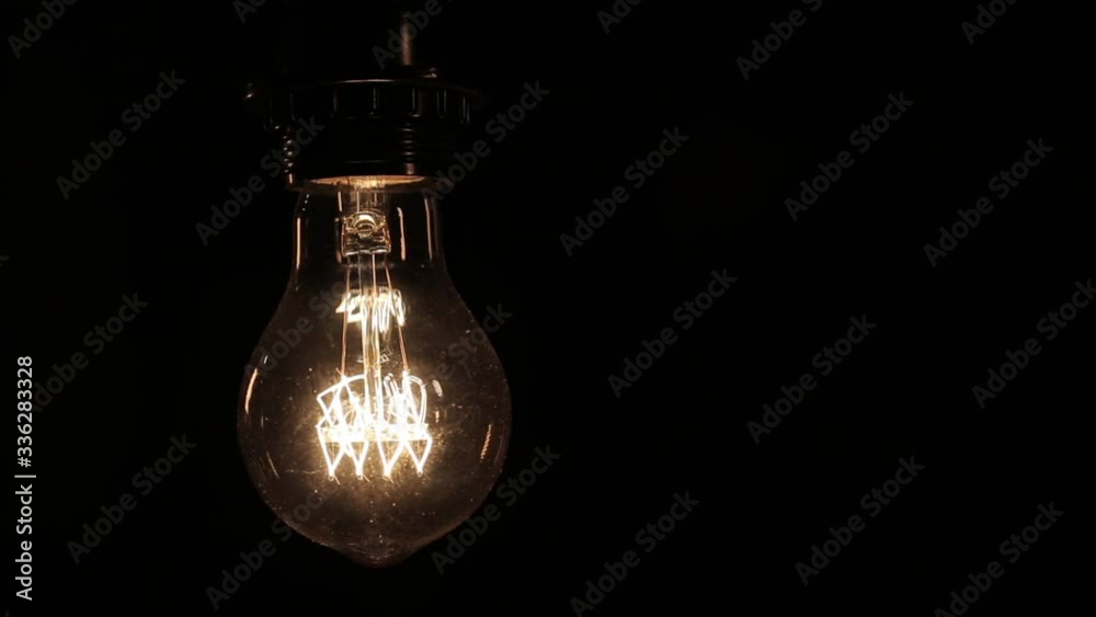 Close-up of the Edison lamp with warm light sways lightly on a black background Close-up of the Edison lamp with warm light sways lightly on a black background