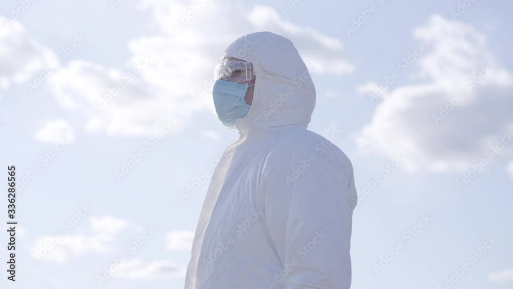 Side view of young Caucasian man putting on protective eyeglasses at the background of sunny spring sky. Virologist in safety suit and face mask standing outdoors during Covid-19 pandemic quarantine. Side view of young Caucasian man putting on protective eyeglasses at the background of sunny spring sky. Virologist in safety suit and face mask standing outdoors during Covid-19 pandemic quarantine.