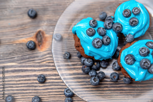 homemade chocolate cupcakes with blue cream and blueberries on a wooden background and transparent plate