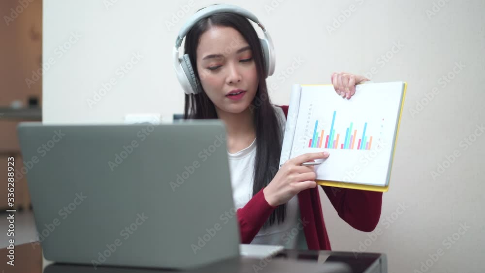 Young Asian female in casual wear working from home showing graph to her coworker via video conference meeting application Young Asian female in casual wear working from home showing graph to her coworker via video conference meeting application