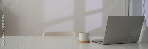 Close up view of workspace with laptop, coffee cup and copy space on white table next to window