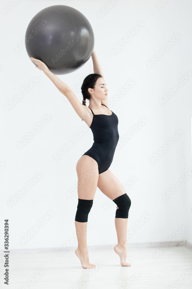 Fototapeta premium Full-length portrait of toned beautiful girl posing in the studio with a fitness ball raised above her head